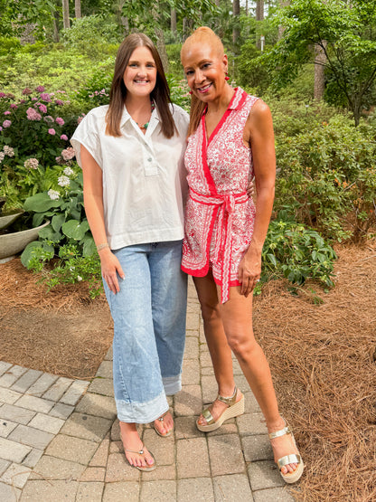 Front view of woman wearing Swagger Boutique’s Red &amp; White Printed Romper by Skies Are Blue with sandals and woman wearing white cap sleeve top walking down a garden path. 