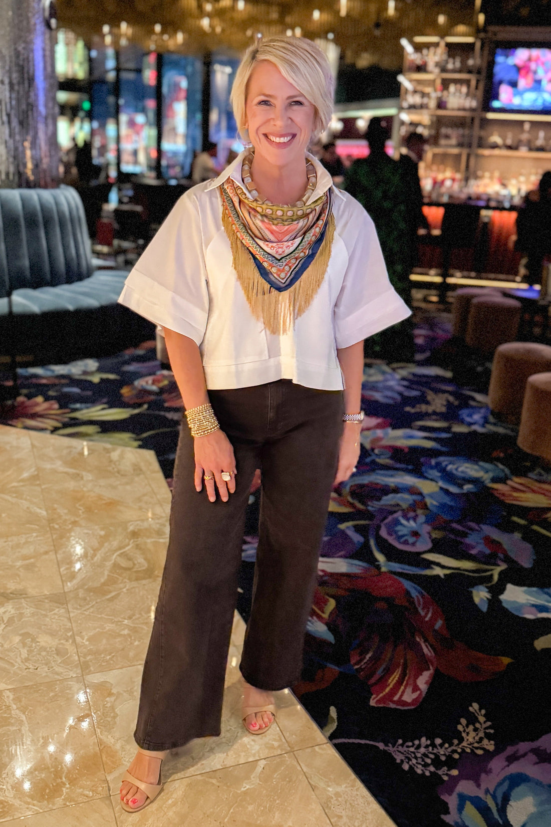 Front view of woman wearing Swagger Boutique’s White Collared Short Sleeve Top with jeans standing inside a bar and restaurant. 