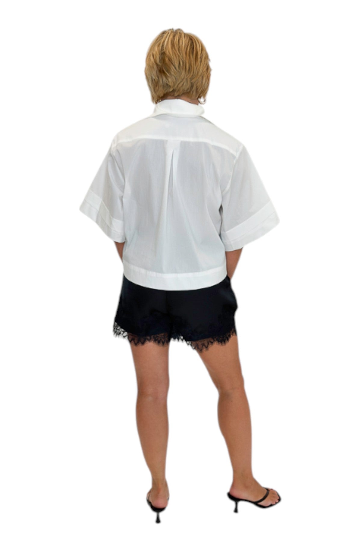 Back view of woman wearing Swagger Boutique’s White Collared Short Sleeve Top with Black Lace Hem Shorts by Entro against white studio background.