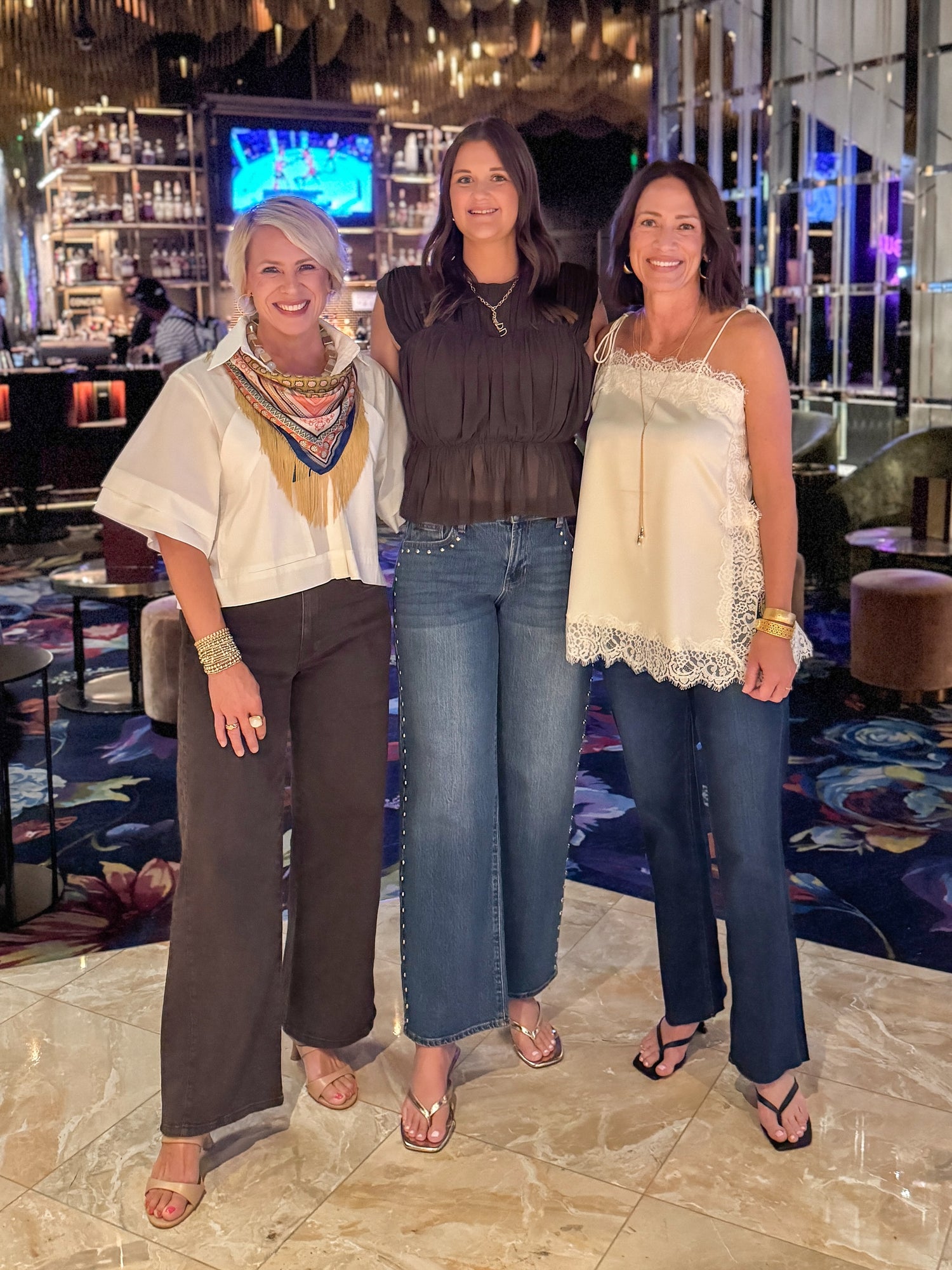 Front view of women wearing Swagger Boutique’s White Collared Short Sleeve Top with jeans and Brown Shirred Peplum Top and Ivory Satin Lace Trim Tank Top by Entro inside of a restaurant.  