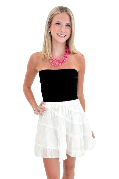 Front view of woman wearing Swagger Boutique’s White Diagonal Seam Mini Skirt with black top against white studio background.