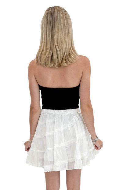 Back view of woman wearing Swagger Boutique’s White Diagonal Seam Mini Skirt with black top against white studio background.