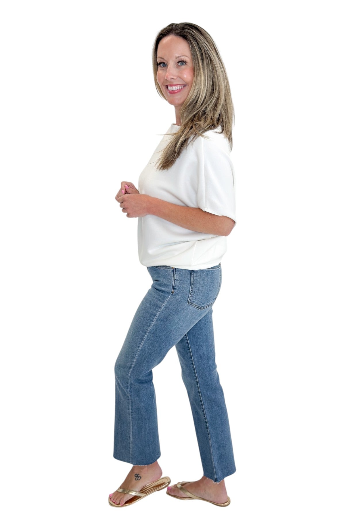 Side view of woman wearing Swagger Boutique’s Off White Dolman Sleeve Top with jeans against white studio background.