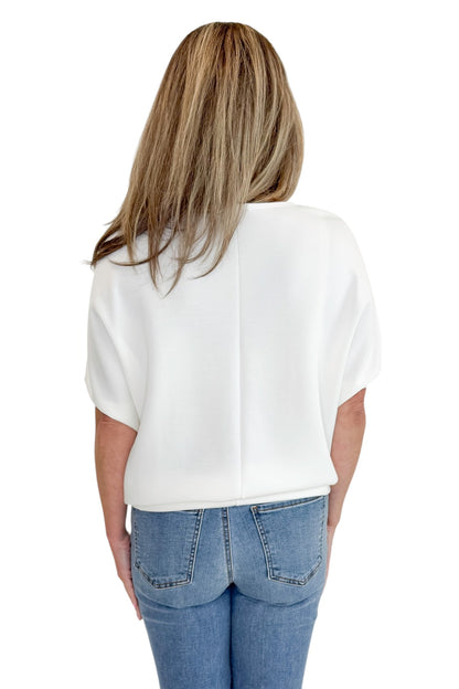 Back view of woman wearing Swagger Boutique’s Off White Dolman Sleeve Top with jeans against white studio background.