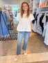 Front view of woman wearing Swagger Boutique’s White Embroidered Peplum Top with jeans at the store. 