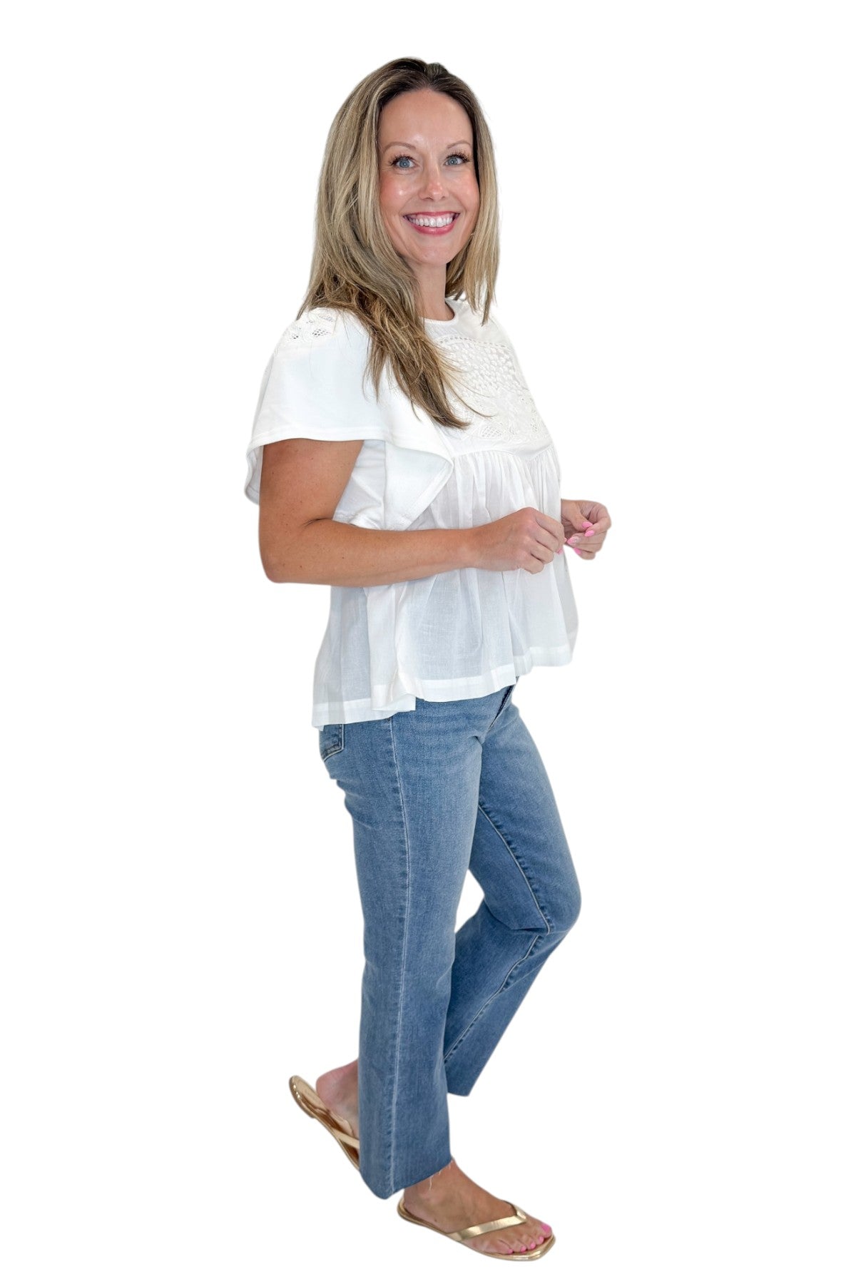 Side view of woman wearing Swagger Boutique’s White Embroidered Peplum Top with jeans against white studio background.