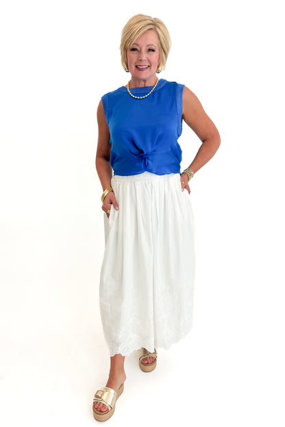 Front view of woman wearing Swagger Boutique’s Blue Sleeveless Tank With Twist by Skies Are Blue with White Embroidered Skirt against white studio background.