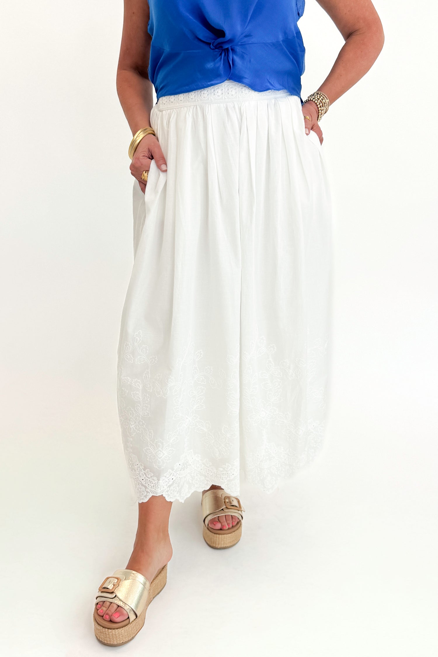 Front view of woman wearing Swagger Boutique’s Blue Sleeveless Tank With Twist by Skies Are Blue with White Embroidered Skirt against white studio background.