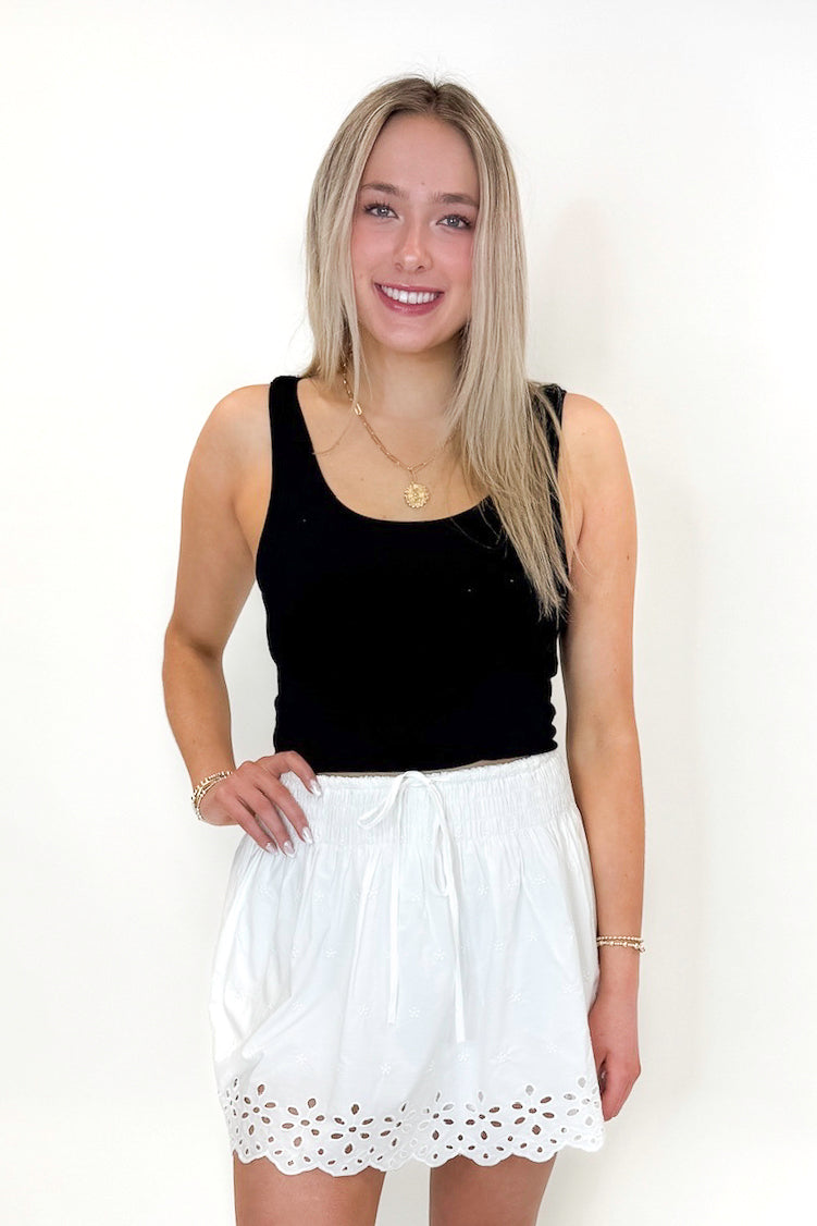 Front view of woman wearing Swagger Boutique’s White Eyelet Skort with black tank against white studio background.