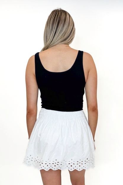 Back view of woman wearing Swagger Boutique’s White Eyelet Skort with black tank against white studio background.