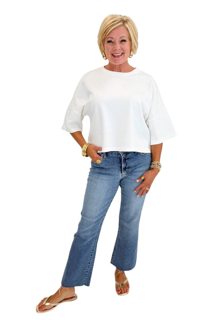 Front view of woman wearing Swagger Boutique’s White Floral Embroidered Short Sleeve Sweatshirt by Entro with jeans against white studio background.
