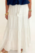 Front detail view of woman wearing Swagger Boutique’s White Flowy Tiered Cotton Skirt with blue top against white studio background.