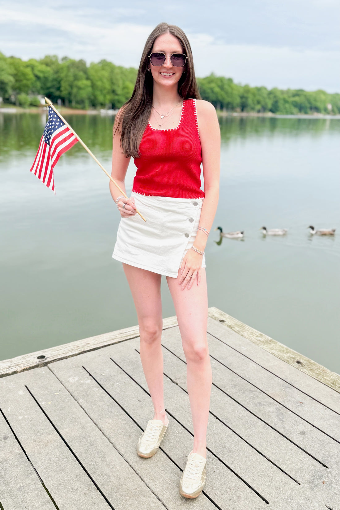 Front view of woman wearing Swagger Boutique’s Red Stitch Detail Sweater Tank with White High Rise Button Down Denim Skort by Risen outside at the lake.