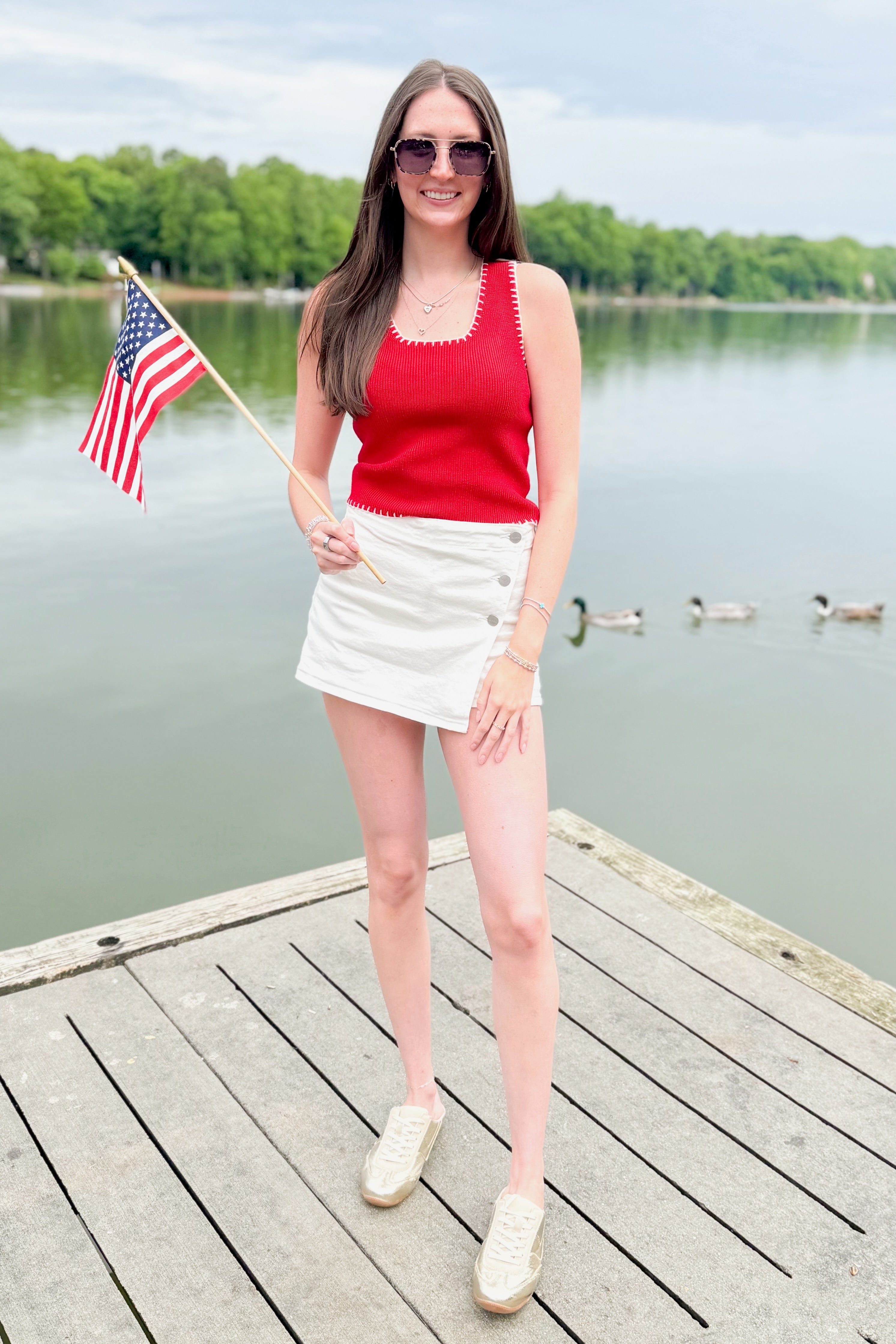 Front view of woman wearing Swagger Boutique’s Red Stitch Detail Sweater Tank with White High Rise Button Down Denim Skort by Risen outside at the lake.