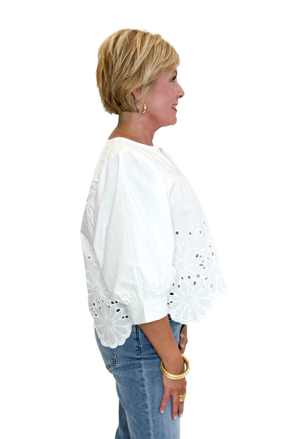 Side view of woman wearing Swagger Boutique’s White Puff Sleeve Eyelet Top with jeans against white studio background.