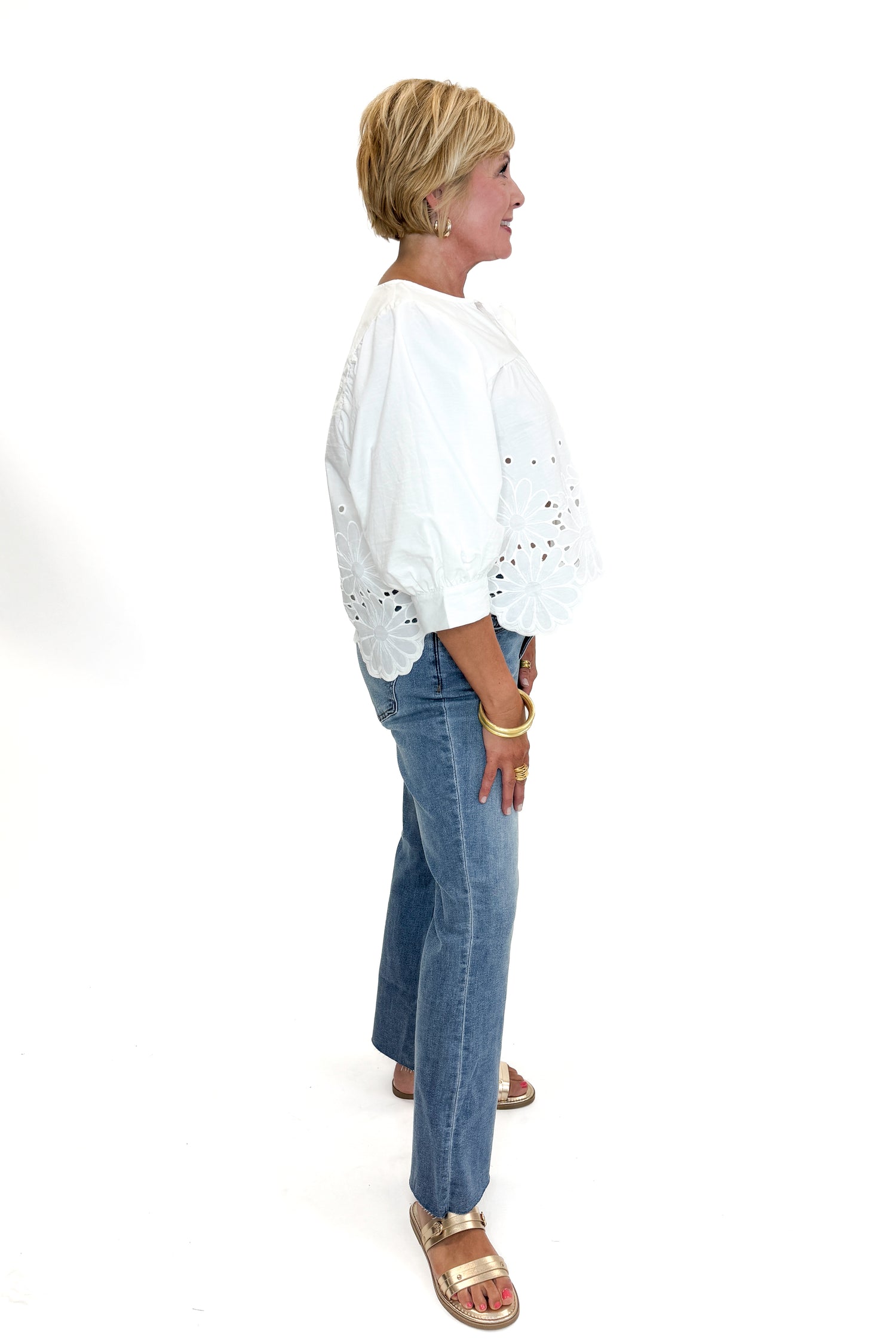 Side view of woman wearing Swagger Boutique’s White Puff Sleeve Eyelet Top with jeans against white studio background.