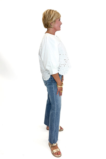 Side view of woman wearing Swagger Boutique’s White Puff Sleeve Eyelet Top with jeans against white studio background.