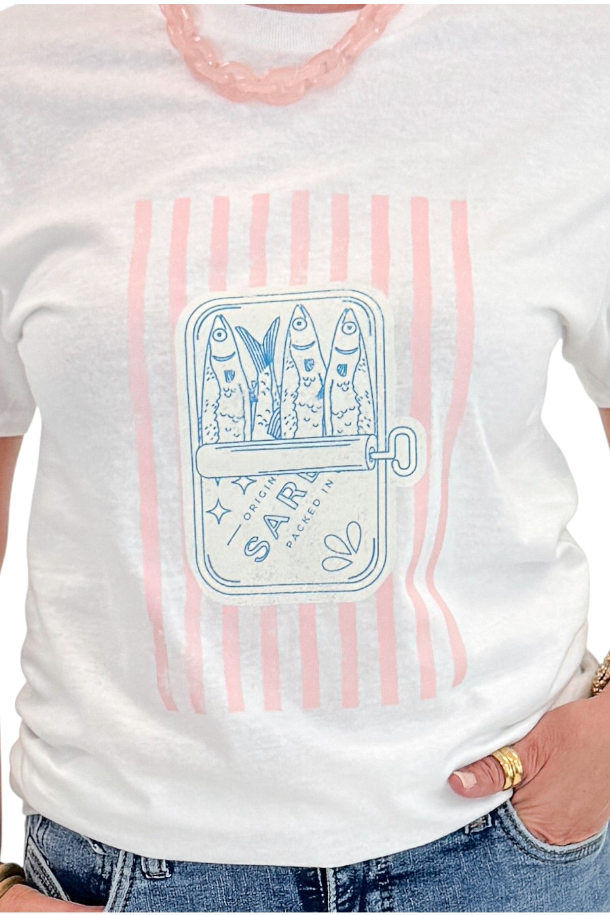 Front detail view of woman wearing Swagger Boutique’s White Sardine Graphic T-Shirt with jeans against white studio background.