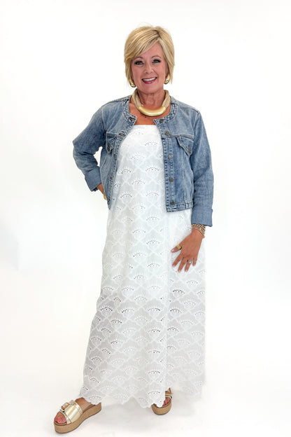 Front view of woman wearing Swagger Boutique’s White Strapless Eyelet Midi Dress by Entro and Medium Wash Collarless Denim Jacket by Just Black Denim with sandals against white studio background.