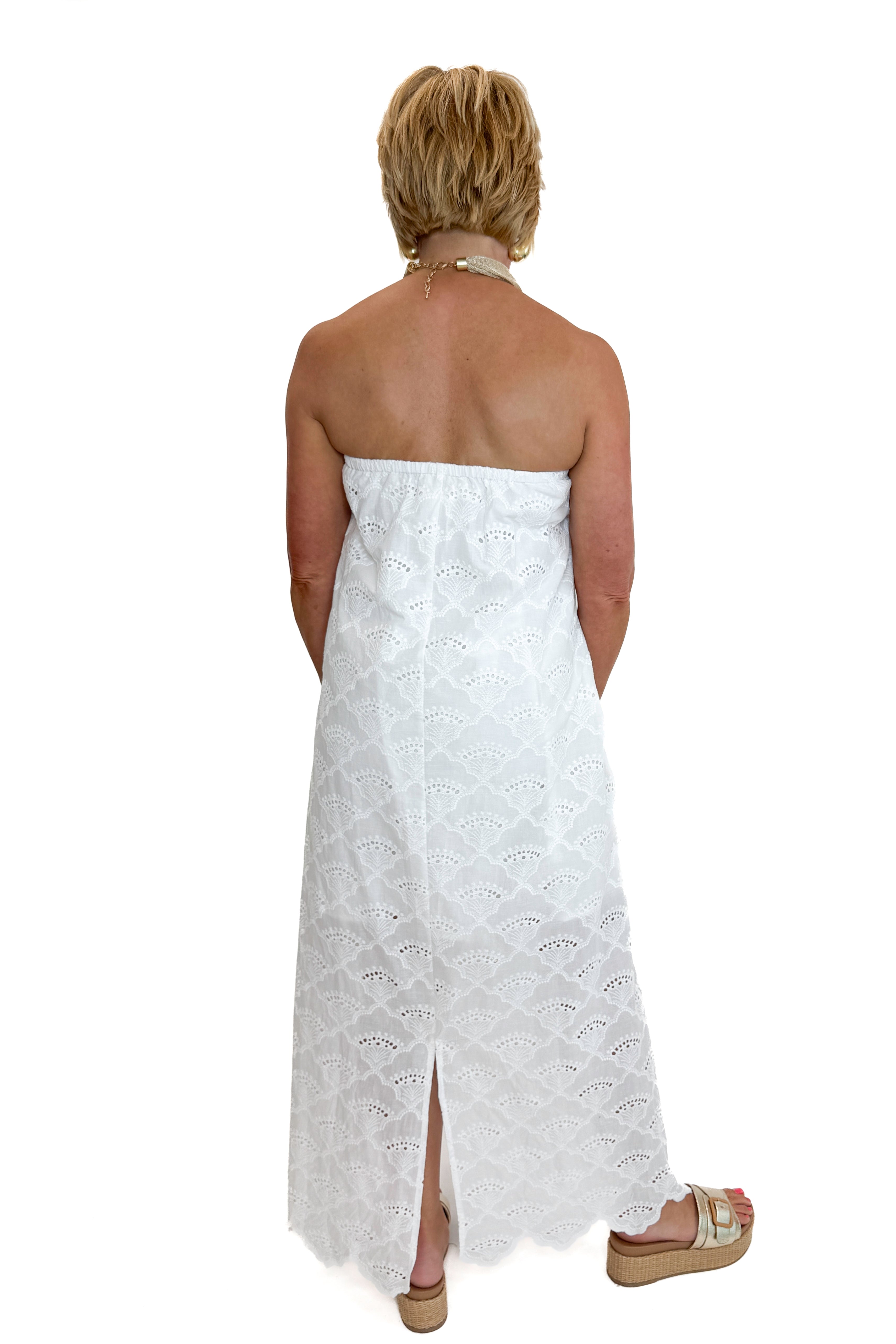 Back view of woman wearing Swagger Boutique’s White Strapless Eyelet Midi Dress by Entro with sandals against white studio background.