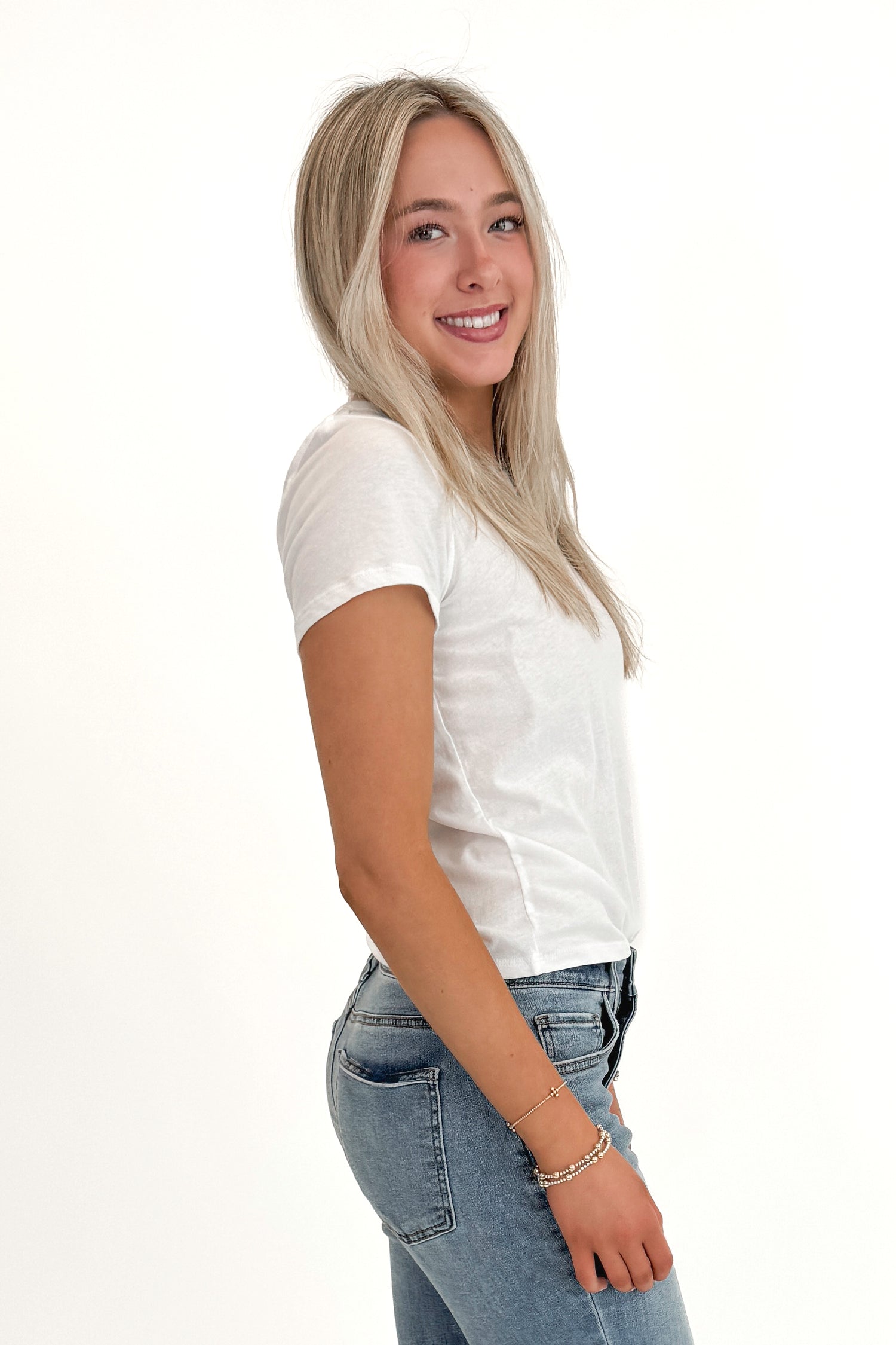 Side view of woman wearing Swagger Boutique’s White Tourist Tee by Z Supply with jeans against white studio background.