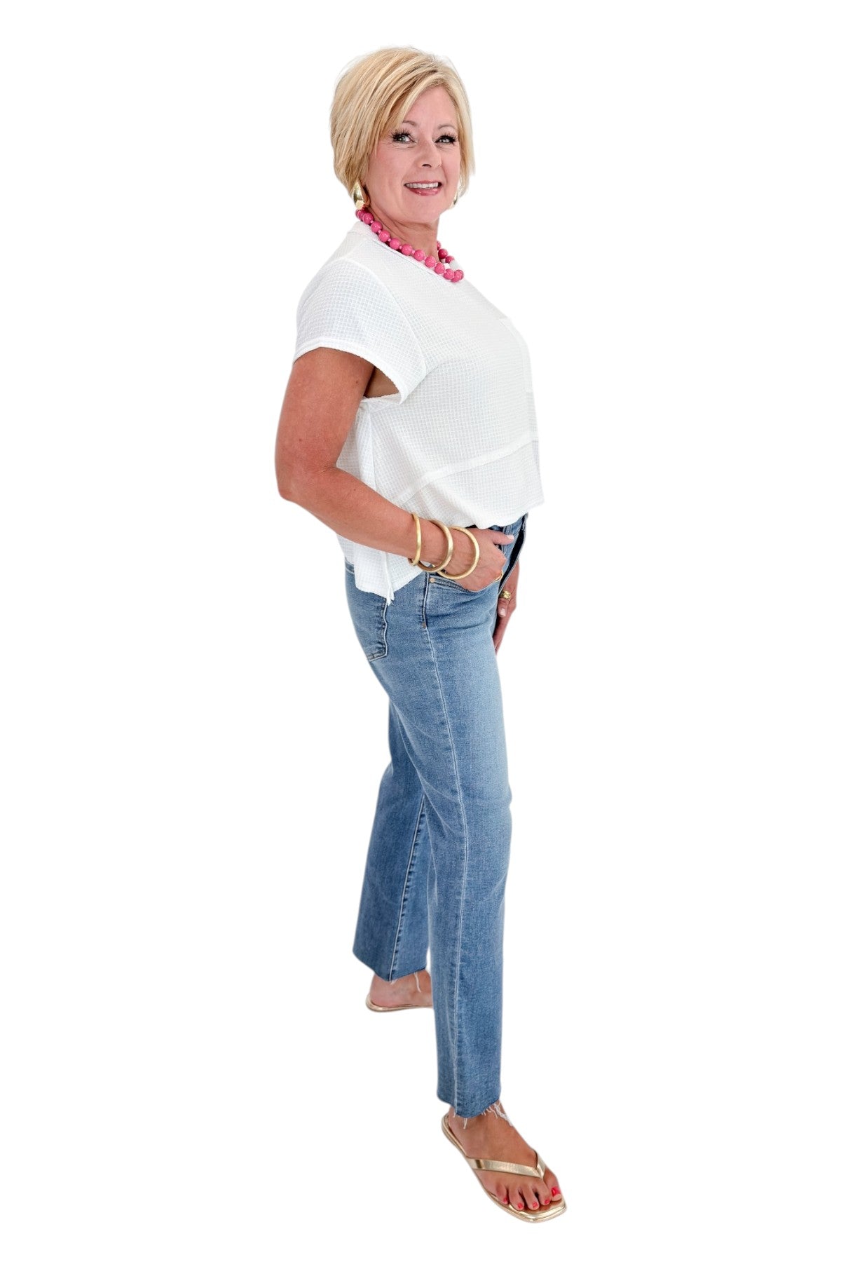 Side view of woman wearing Swagger Boutique’s White Waffle Knit Tee with jeans against white studio background.