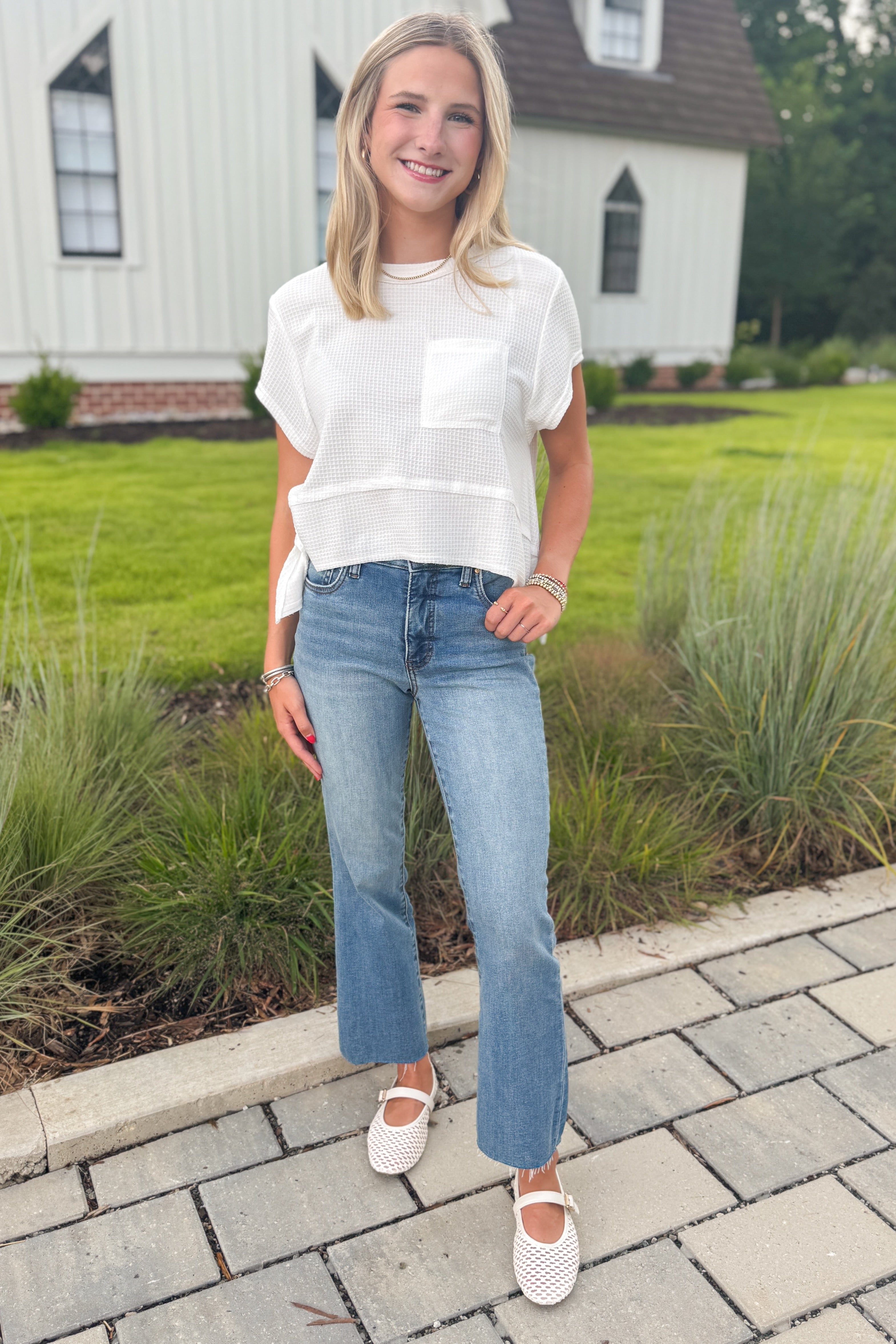 Front view of woman wearing Swagger Boutique’s White Waffle Knit Tee with jeans standing outside by a yard. 