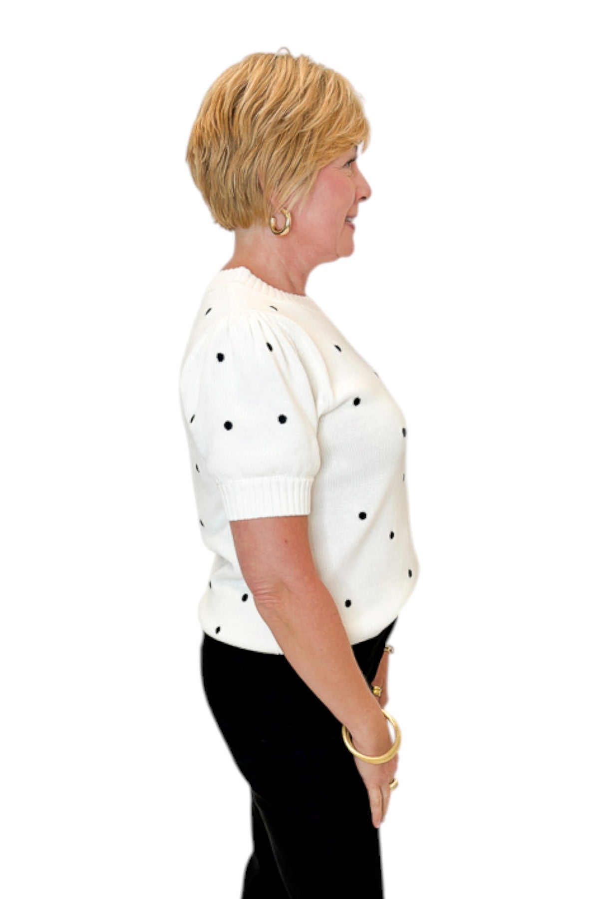 Side view of woman wearing Swagger Boutique’s White With Black Polka Dot Short Sleeve Sweater with jeans against white studio background.