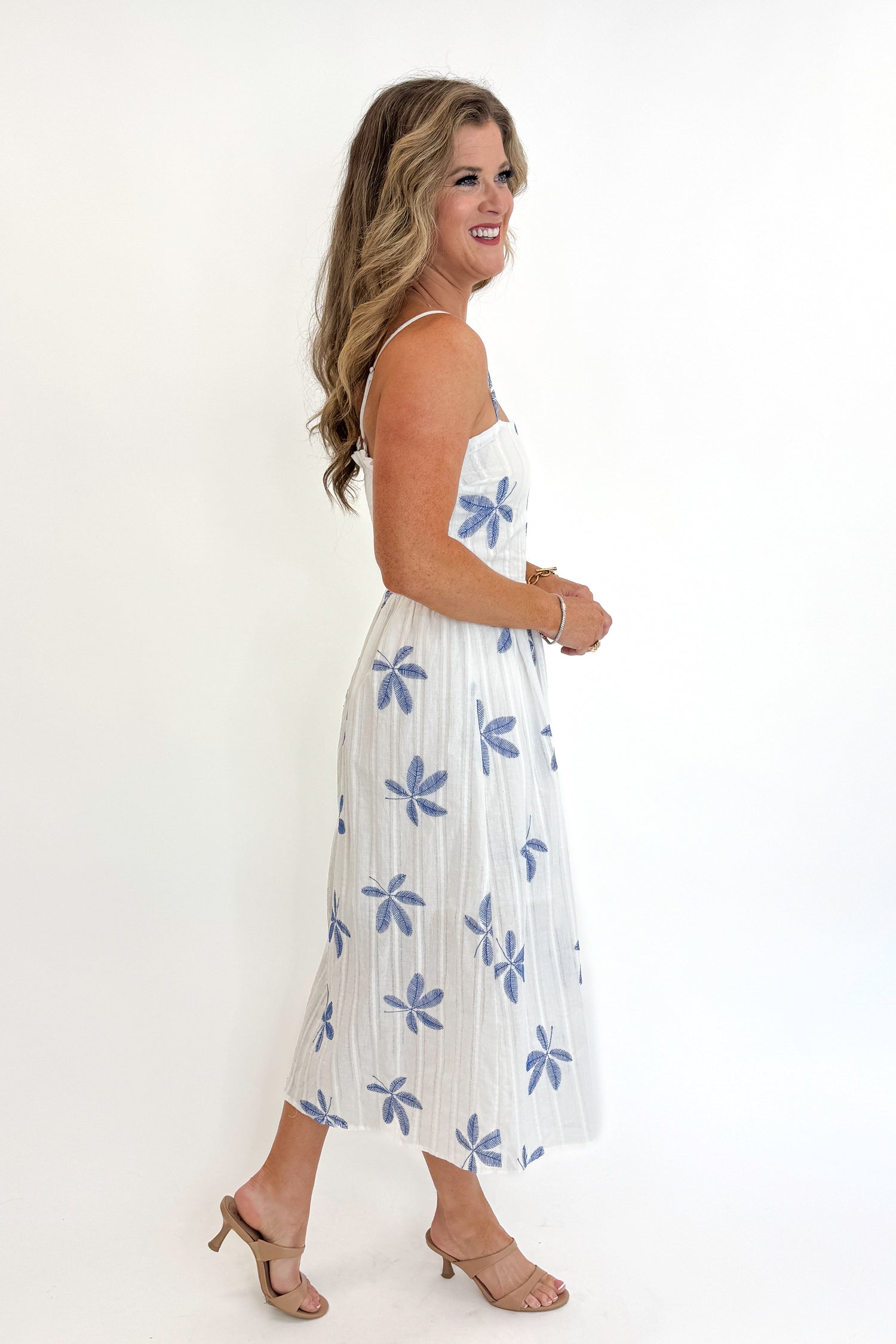 Side view of woman wearing Swagger Boutique’s White With Blue Embroidery Midi Dress against white studio background.