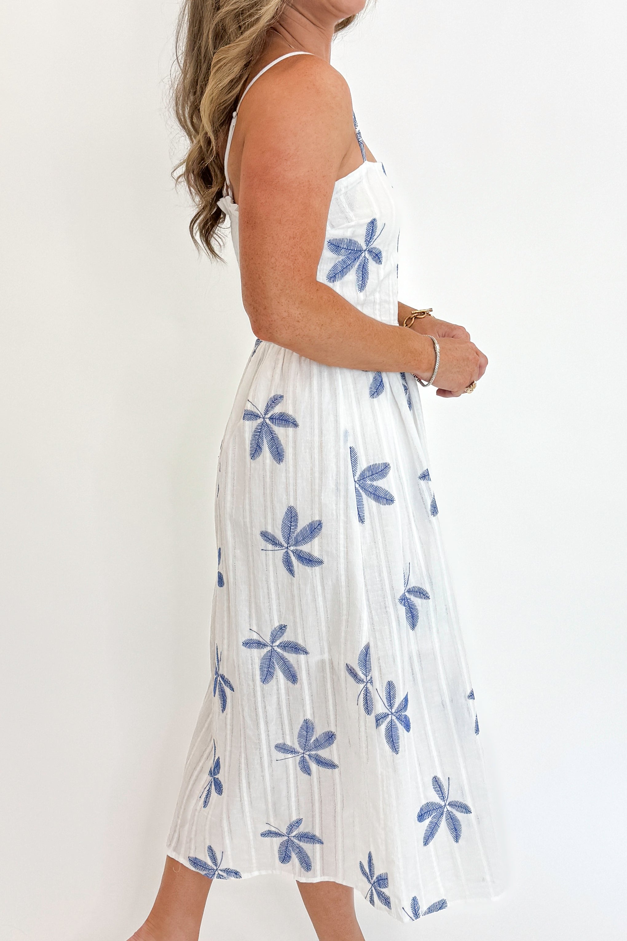 Side detail view of woman wearing Swagger Boutique’s White With Blue Embroidery Midi Dress against white studio background.