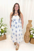 Front view of woman wearing Swagger Boutique’s White With Blue Embroidery Midi Dress with sandals against decorative background.
