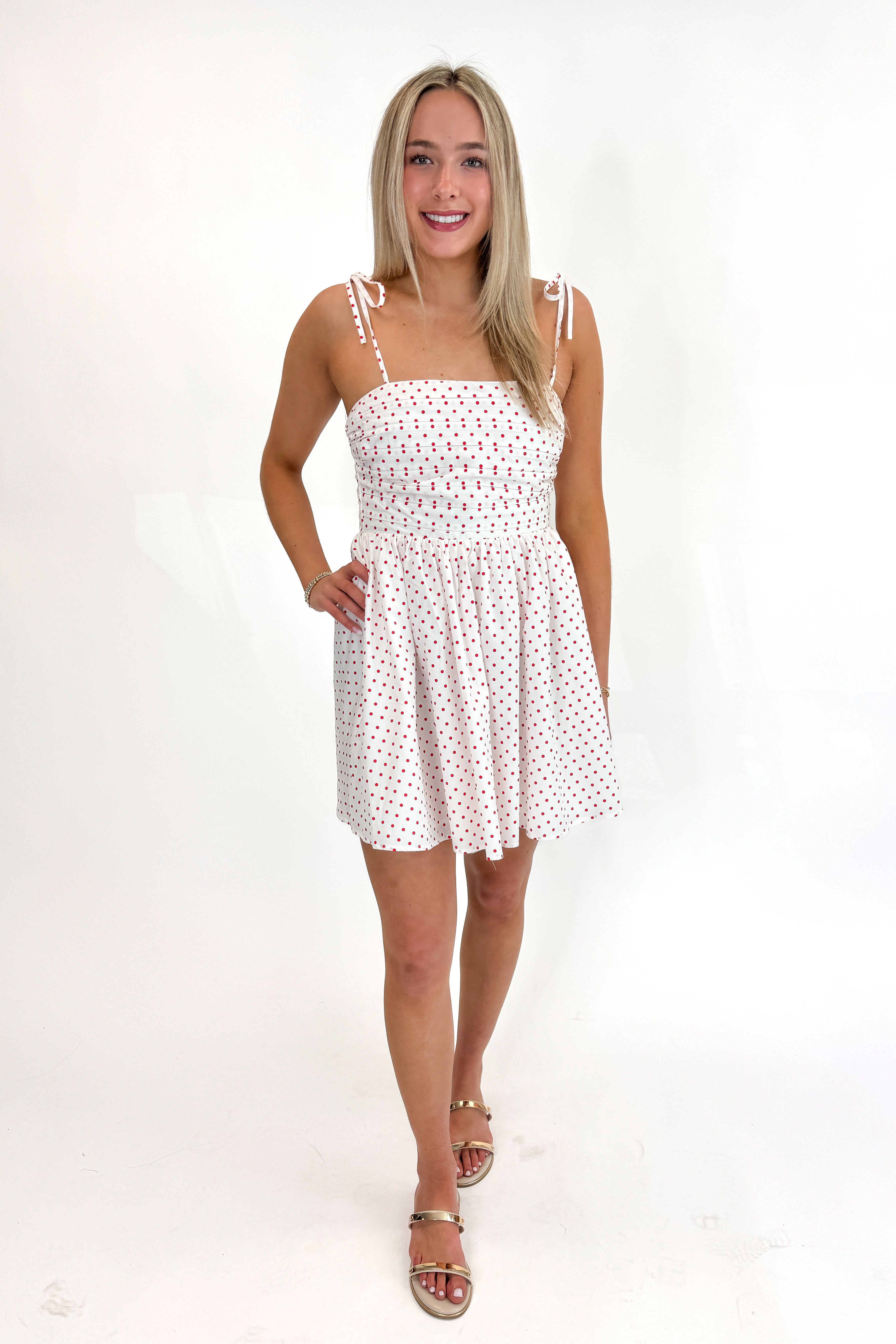 Front view of woman wearing Swagger Boutique’s White With Red Polka Dots Tie Strap Dress with sandals against white studio background.