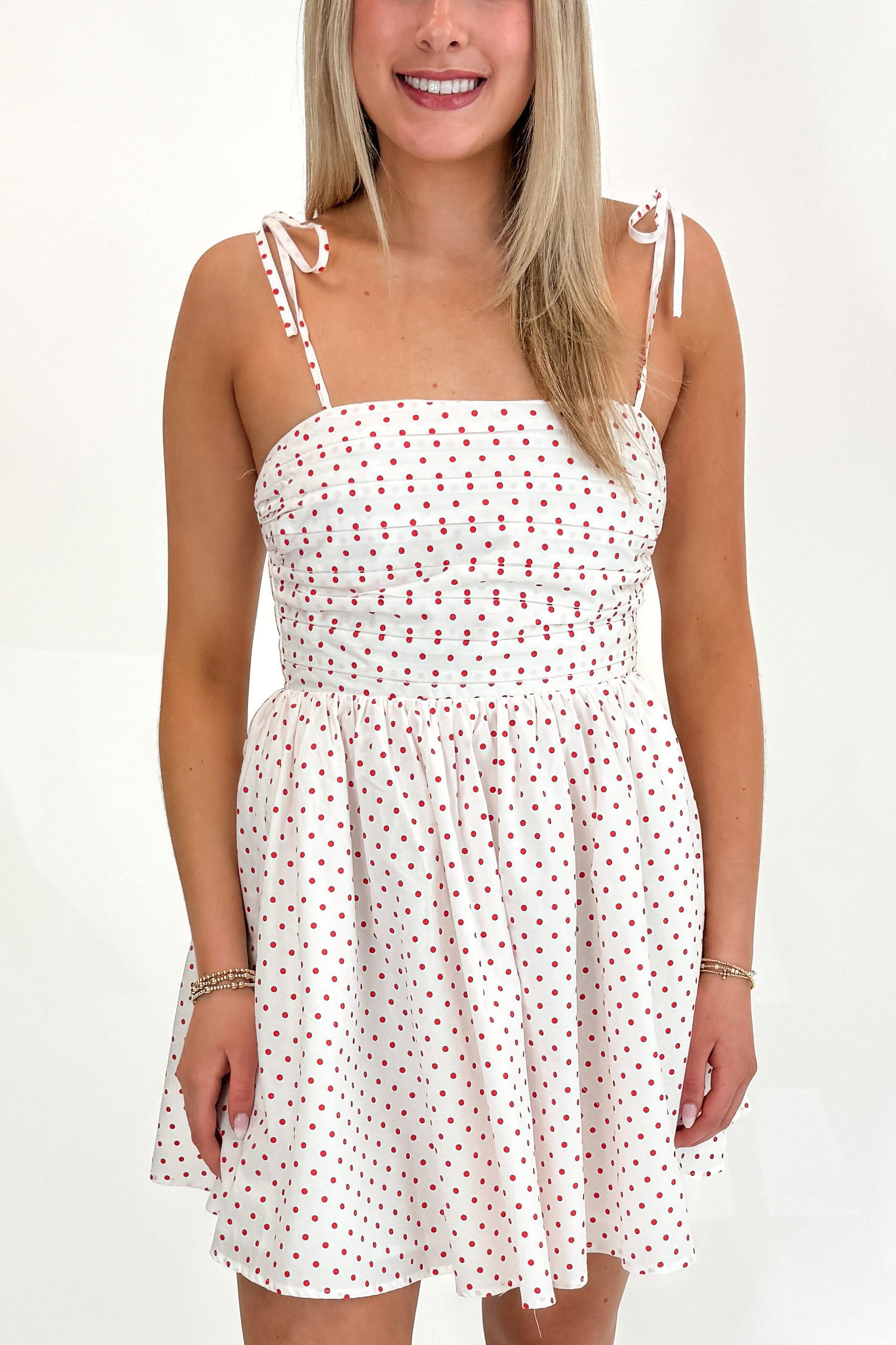 Front detail view of woman wearing Swagger Boutique’s White With Red Polka Dots Tie Strap Dress with sandals against white studio background.