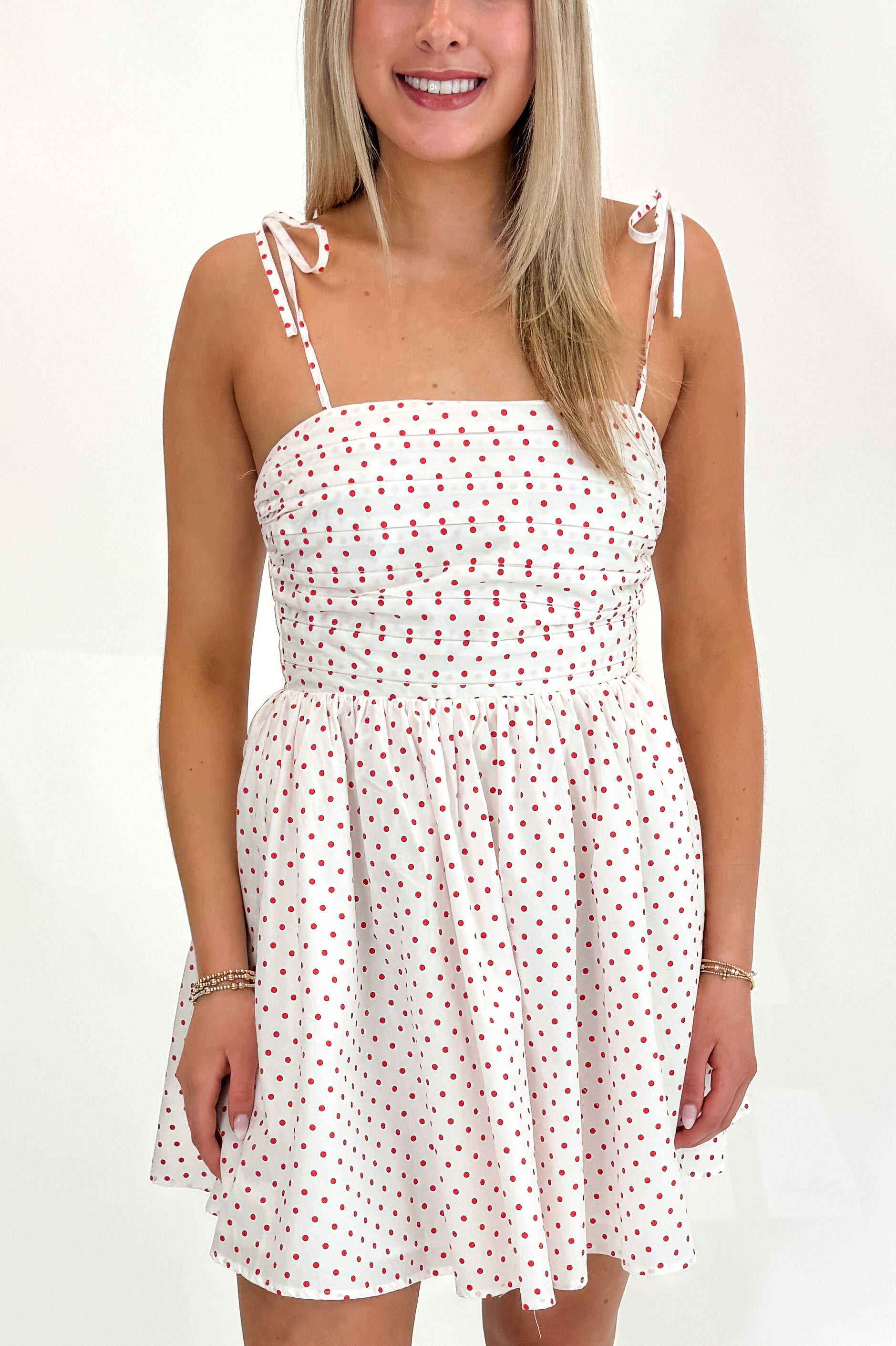 Front detail view of woman wearing Swagger Boutique’s White With Red Polka Dots Tie Strap Dress with sandals against white studio background.