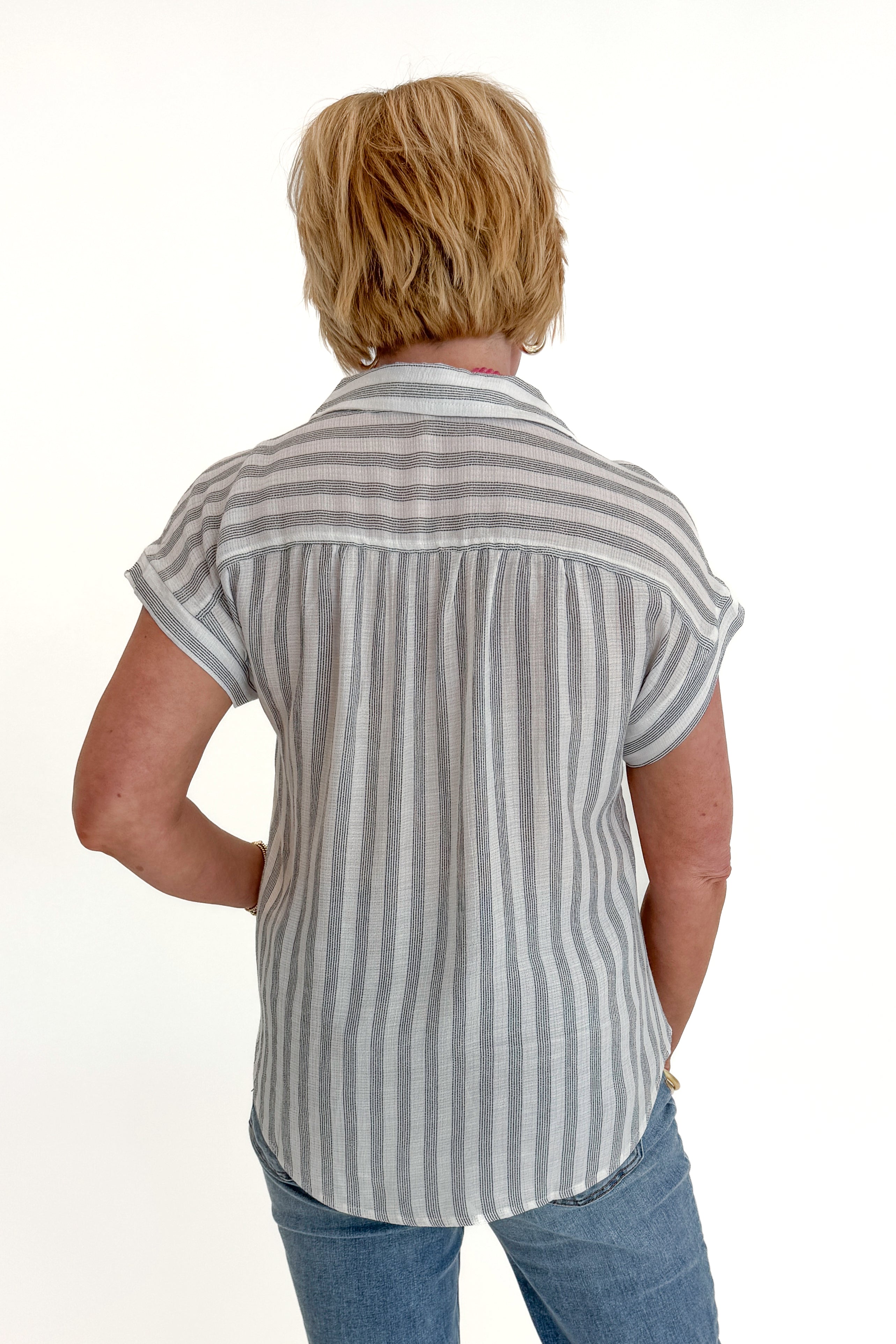 Back view of woman wearing Swagger Boutique’s White &amp; Black Striped Collared Top with jeans and Kaylie necklace against white studio background.