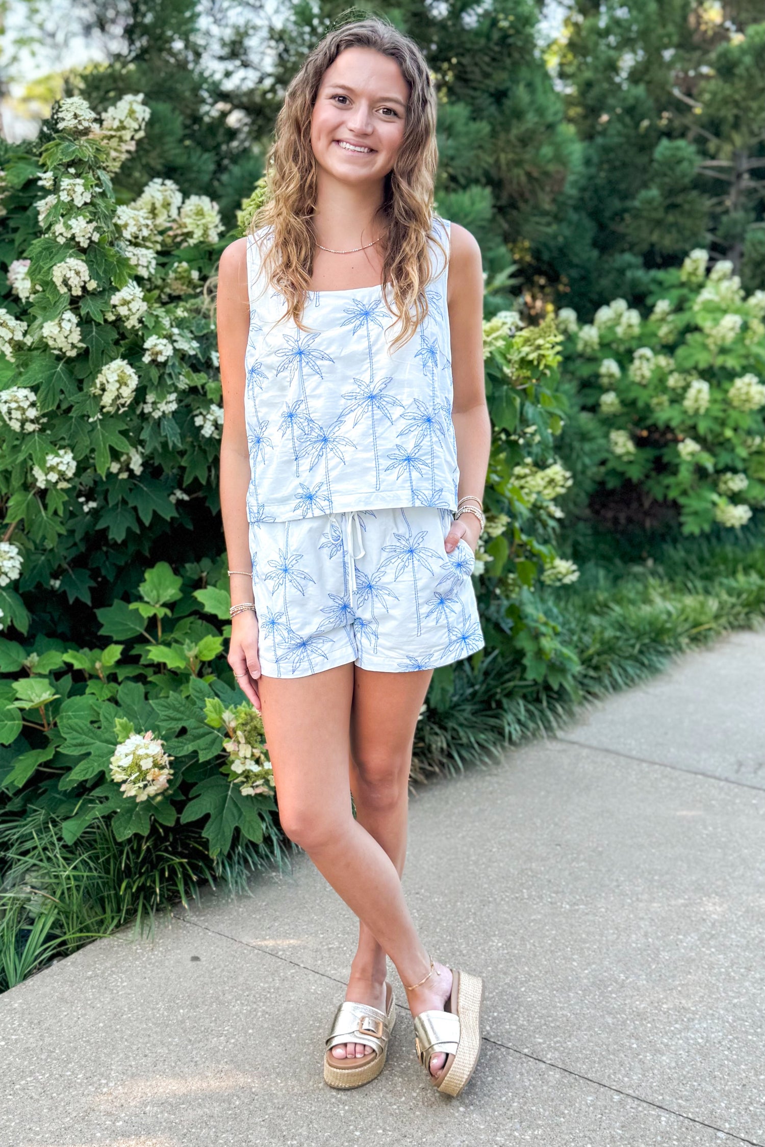 Front view of woman wearing Swagger Boutique’s White &amp; Blue Palm Embroidered Tank &amp; Shorts walking outside.