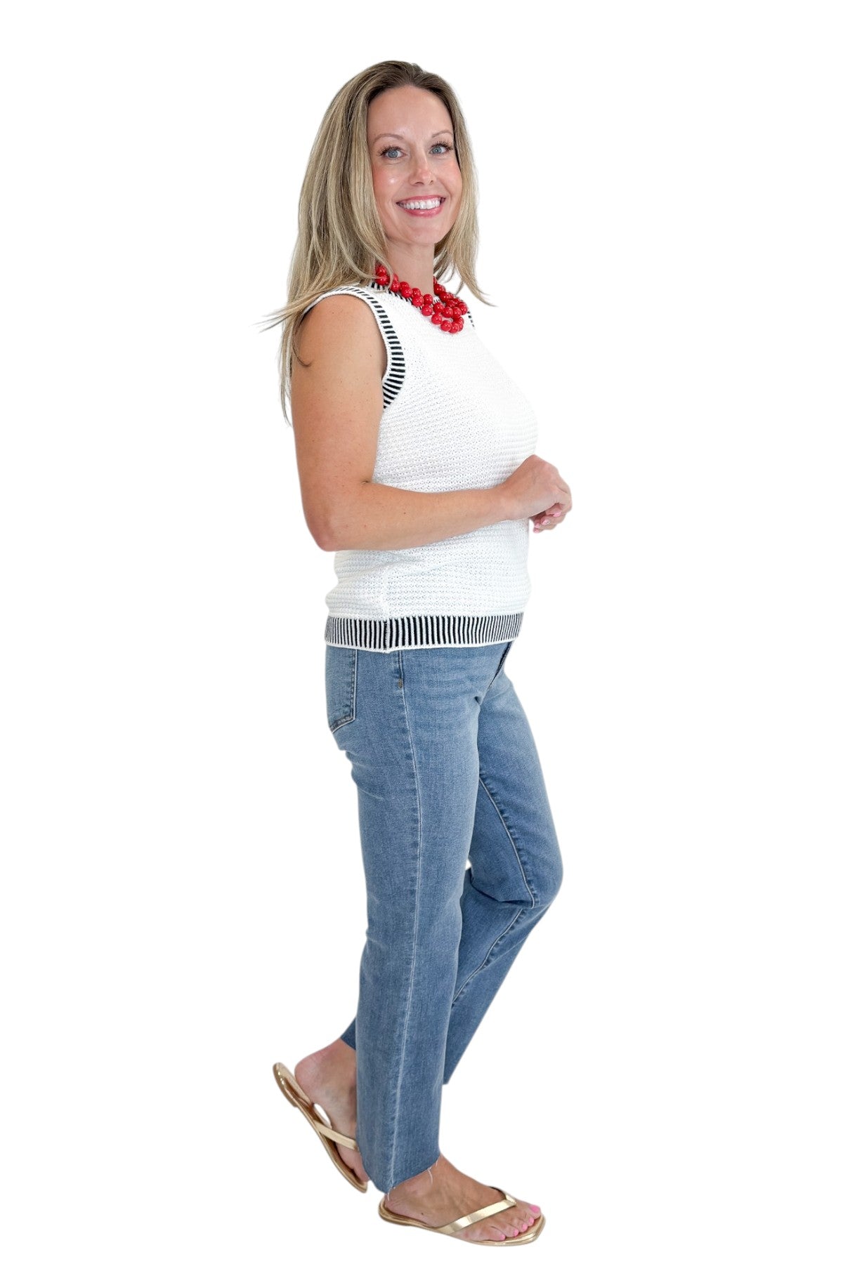 Side view of woman wearing Swagger Boutique’s White &amp; Navy Textured Sweater Tank with jeans against white studio background.