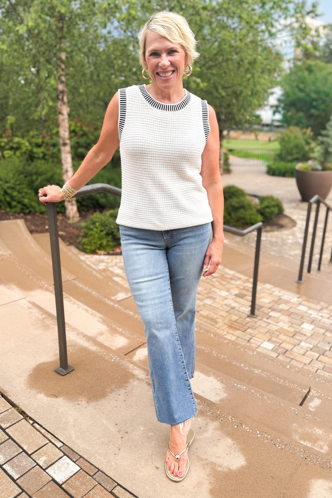 Front view of woman wearing Swagger Boutique’s White &amp; Navy Textured Sweater Tank with jeans leaning against a railing outside.