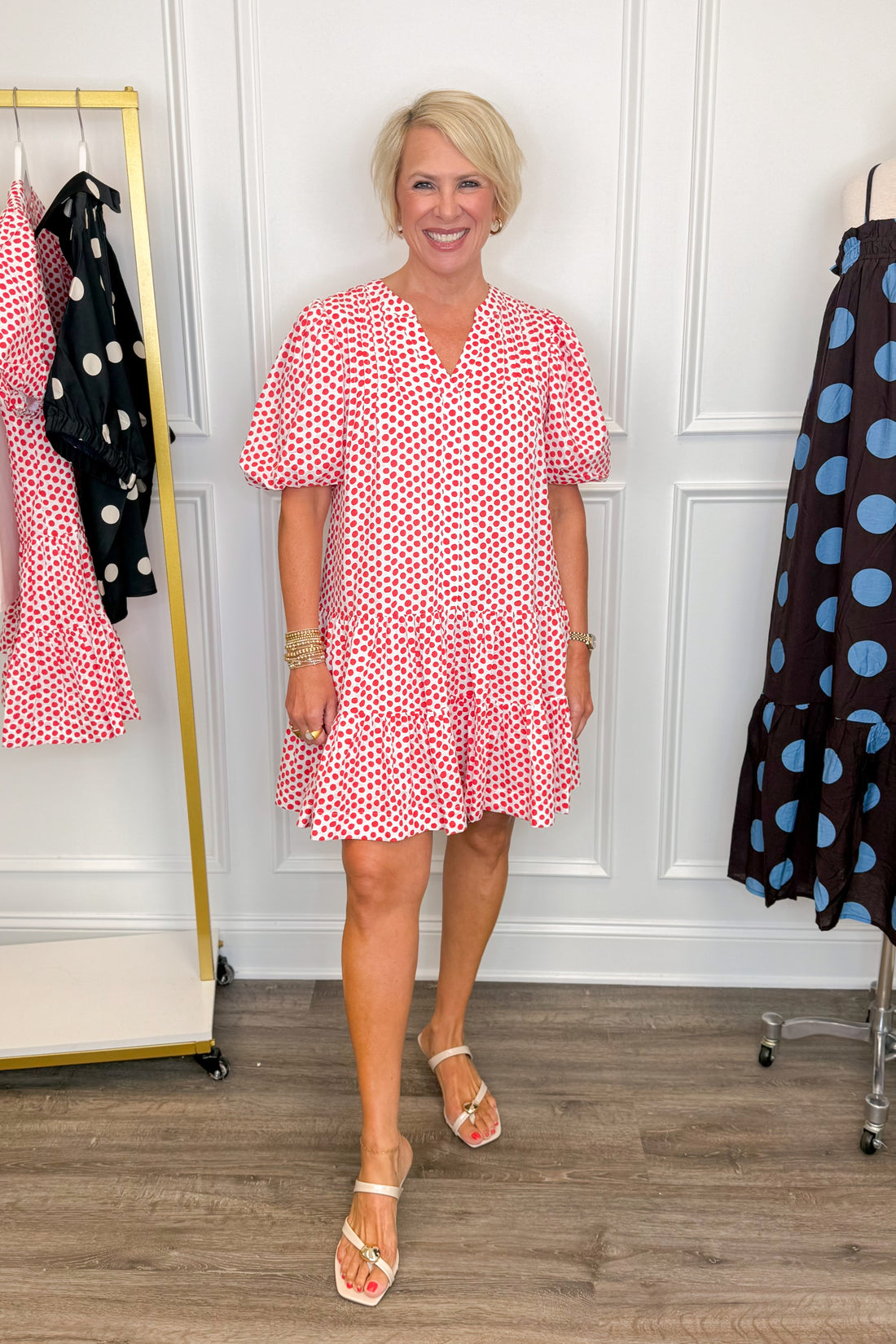 Front view of woman wearing Swagger Boutique’s White &amp; Red Polka Dot Mini Dress with clothing hanging in the background.
