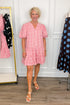 Front view of woman wearing Swagger Boutique’s White & Red Polka Dot Mini Dress with clothing hanging in the background.