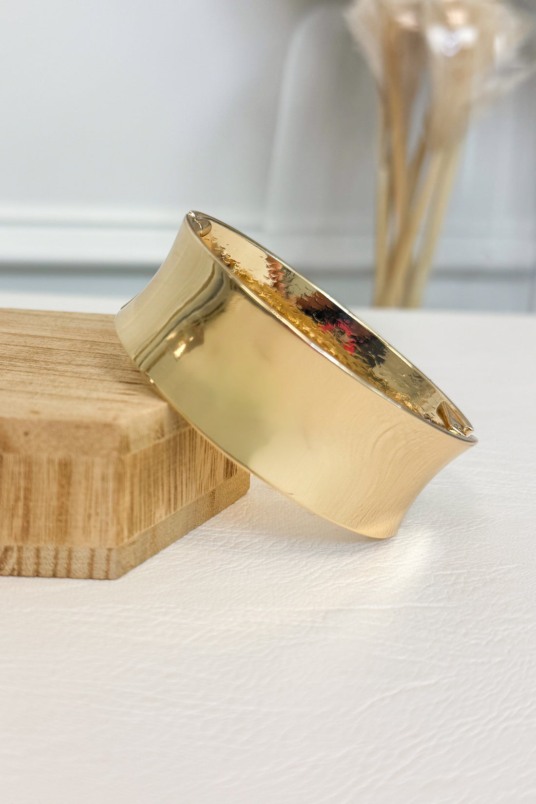 Gold-tone wide bracelet featuring a smooth rounded band on a white studio background