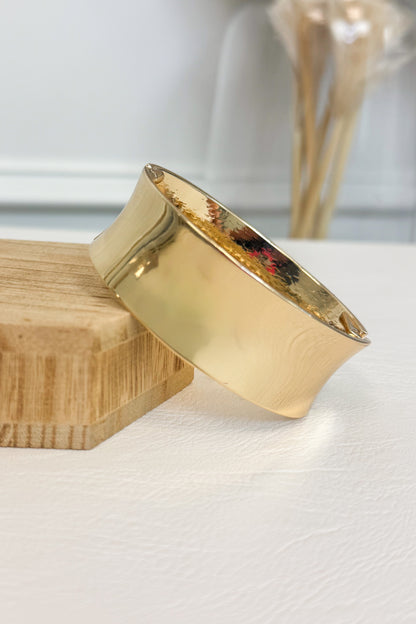 Gold-tone wide bracelet featuring a smooth rounded band on a white studio background