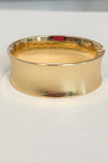 Gold-tone wide polished bracelet with a rounded band design and smooth finish on a white studio background