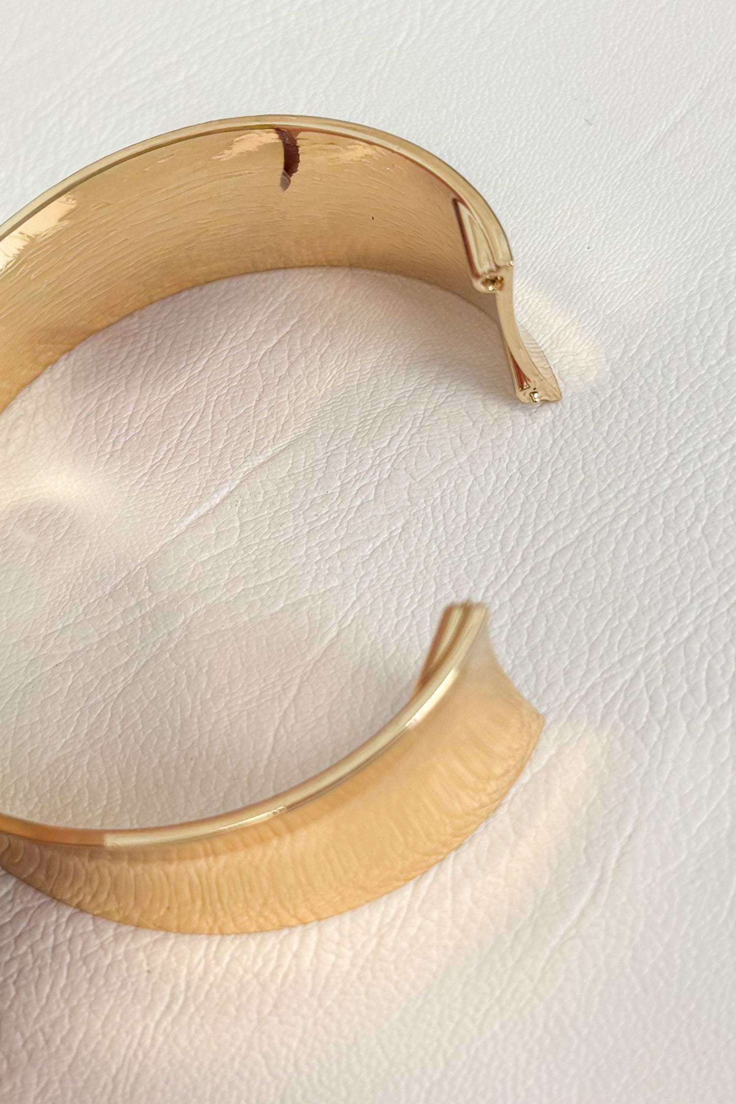 Gold-tone open cuff bracelet with a smooth curved band and polished finish on a white studio background
