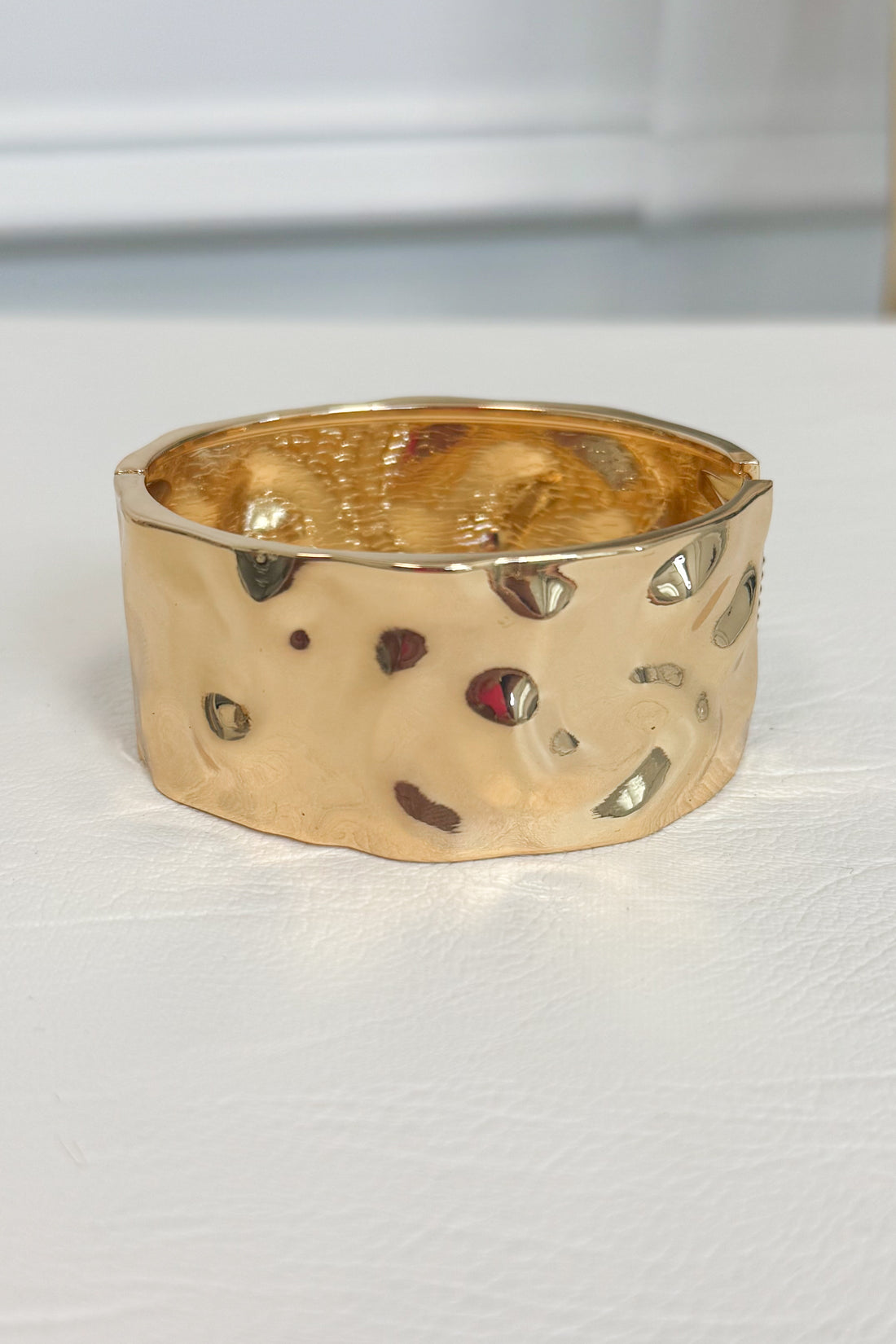 Gold-tone wide bracelet with a textured surface with  embossed and debossed parts on a white studio background