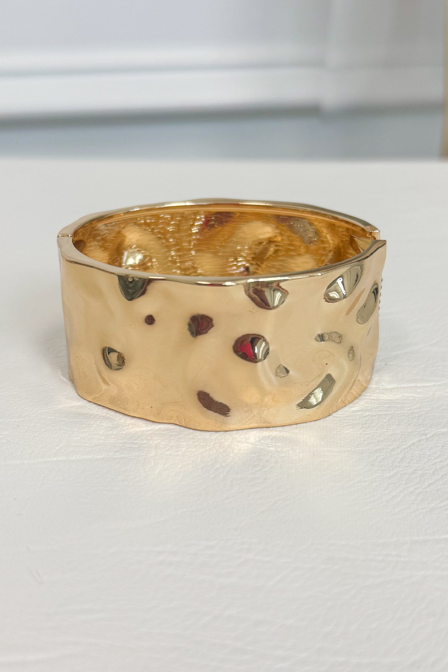Gold-tone wide bracelet with a textured surface with  embossed and debossed parts on a white studio background