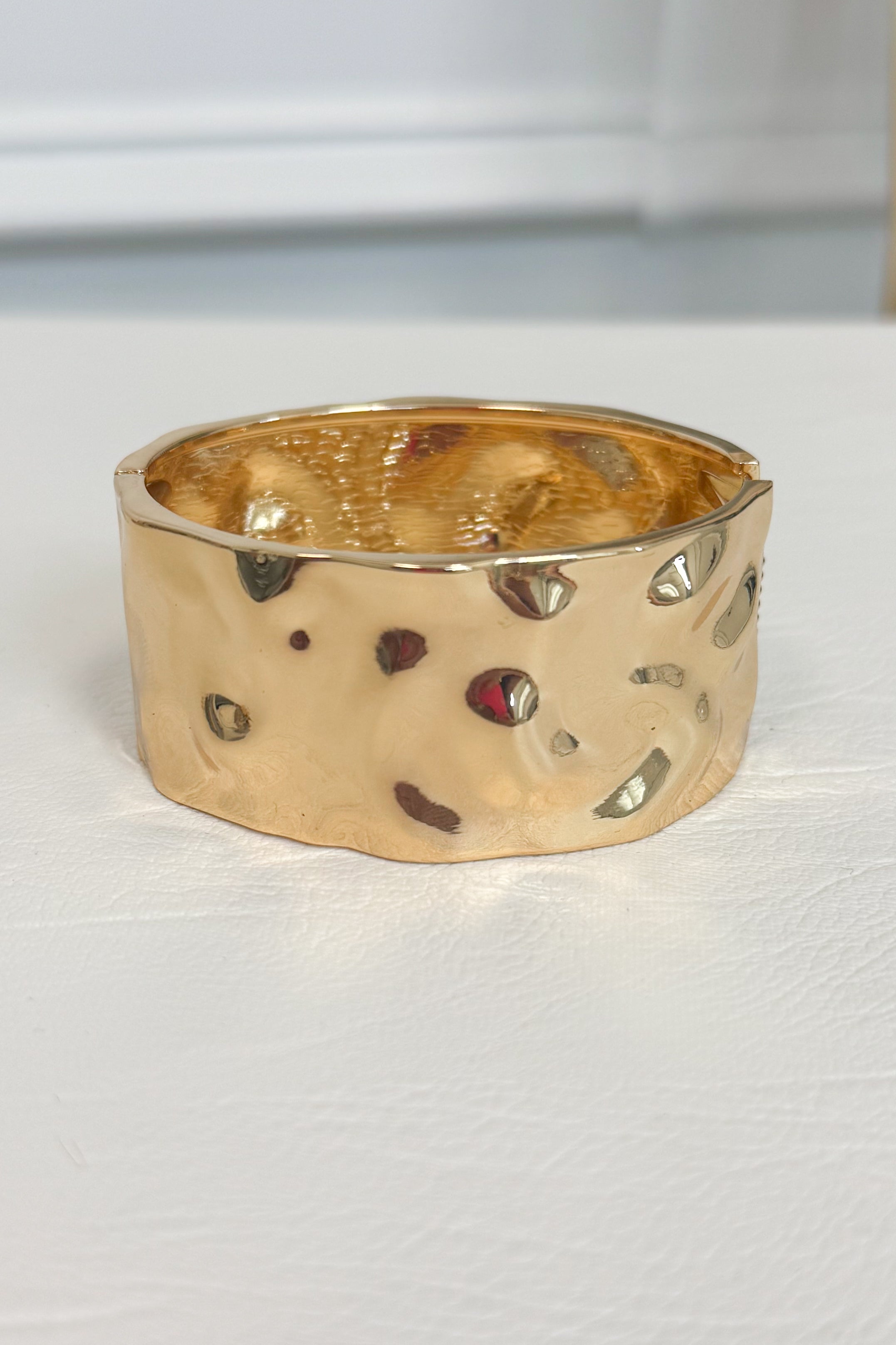 Gold-tone wide bracelet with a textured surface with  embossed and debossed parts on a white studio background