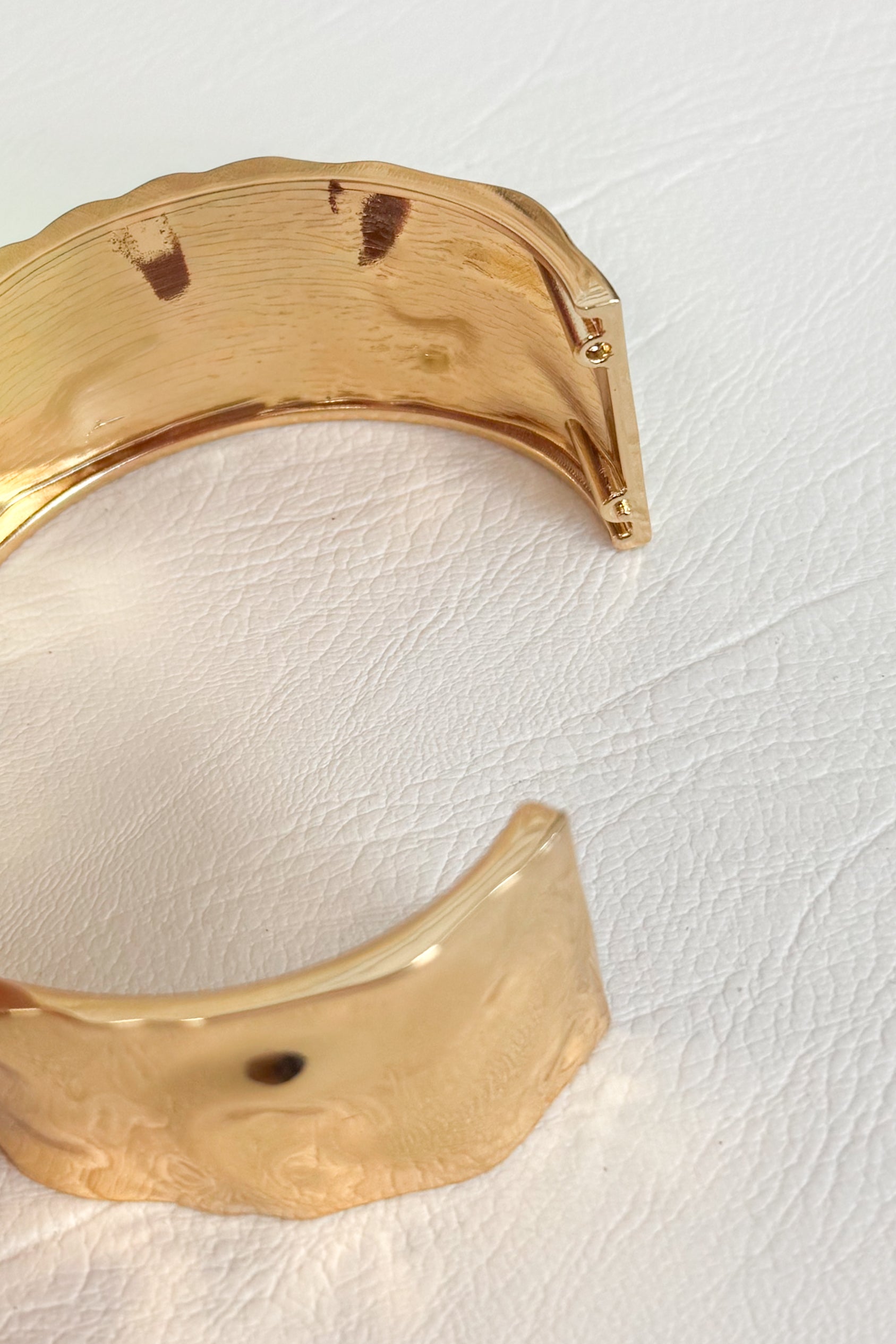 Gold-tone open cuff bracelet with a wide curved band on a white studio background