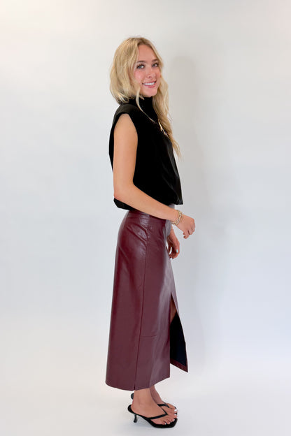 Side view of woman wearing Swagger Boutique’s Wine Faux Leather Slit Midi Skirt with black sweater against white studio background.