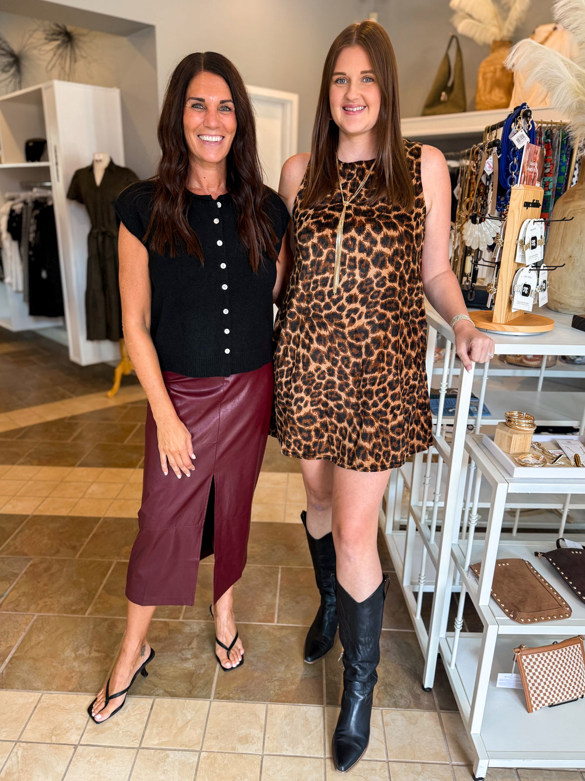 Front view of women wearing Swagger Boutique’s Leopard Velvet Mini Dress with boots and Wine Faux Leather Slit Midi Skirt standing together at the store.
